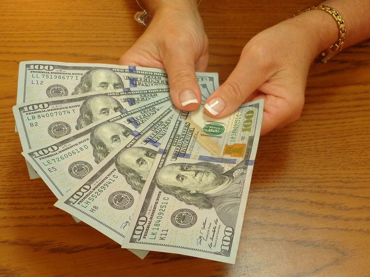A hand holding a fanned-out stack of US banknotes.