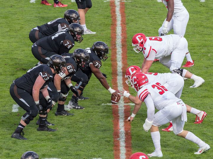 Two college football teams set at the line of scrimmage, both lines crouched over the ball.