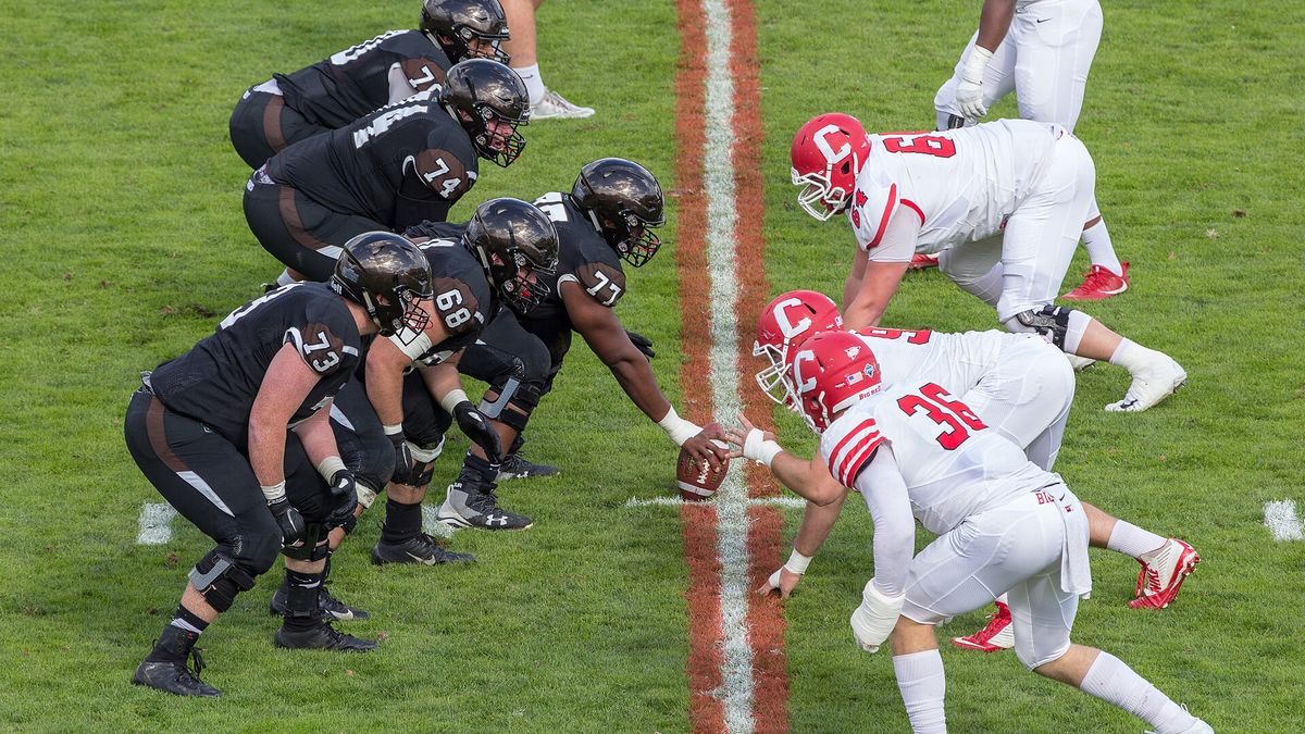Two college football teams set at the line of scrimmage, both lines crouched over the ball.