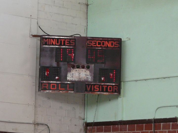 A scoreboard clock on a gym wall, counting minutes and seconds for home and visitor.