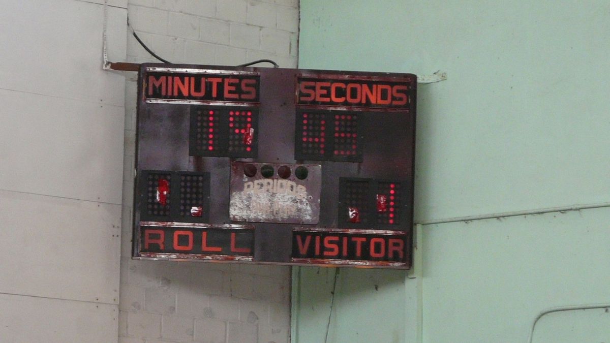 A scoreboard clock on a gym wall, counting minutes and seconds for home and visitor.